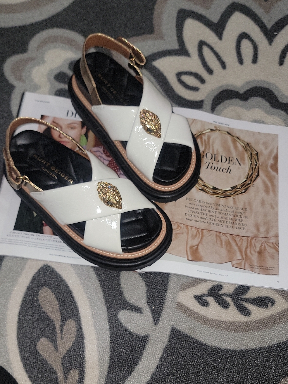 Kurt Geiger White Patent Leather Cross-Strap Sandals with Gold Accent Medallion.